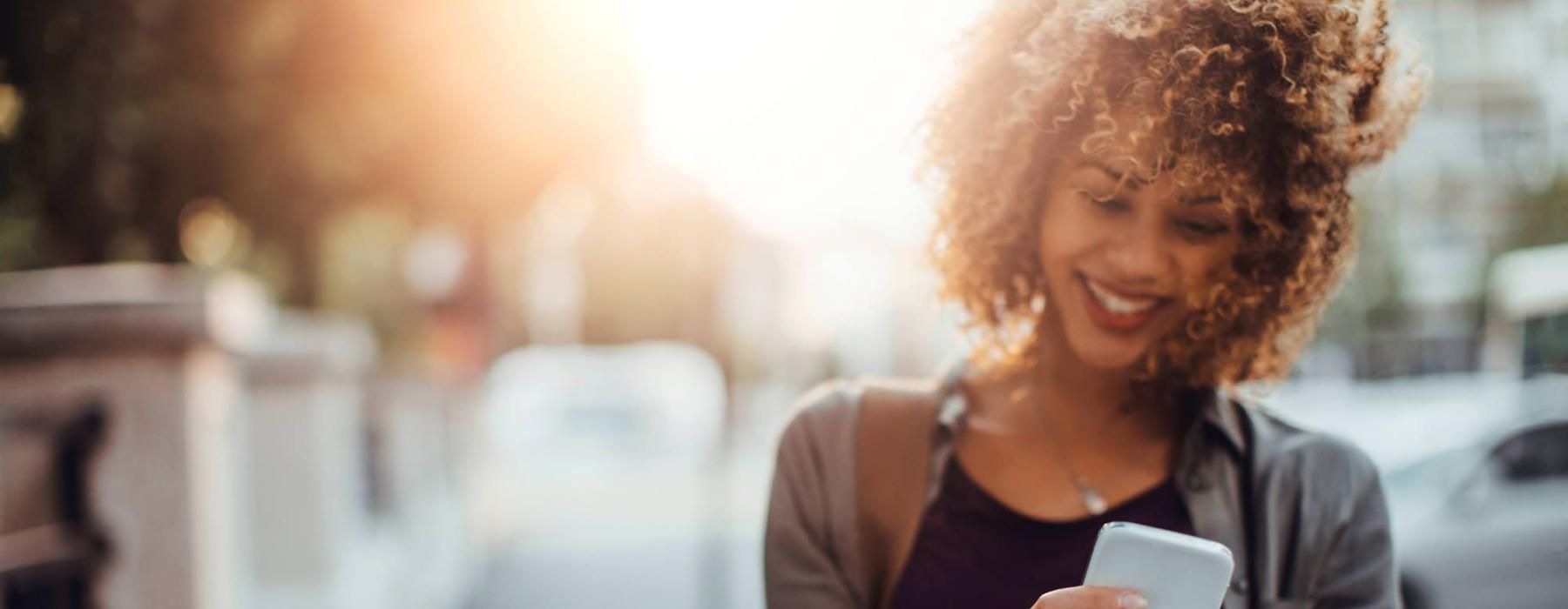 woman texts on her phone as she walks through the city